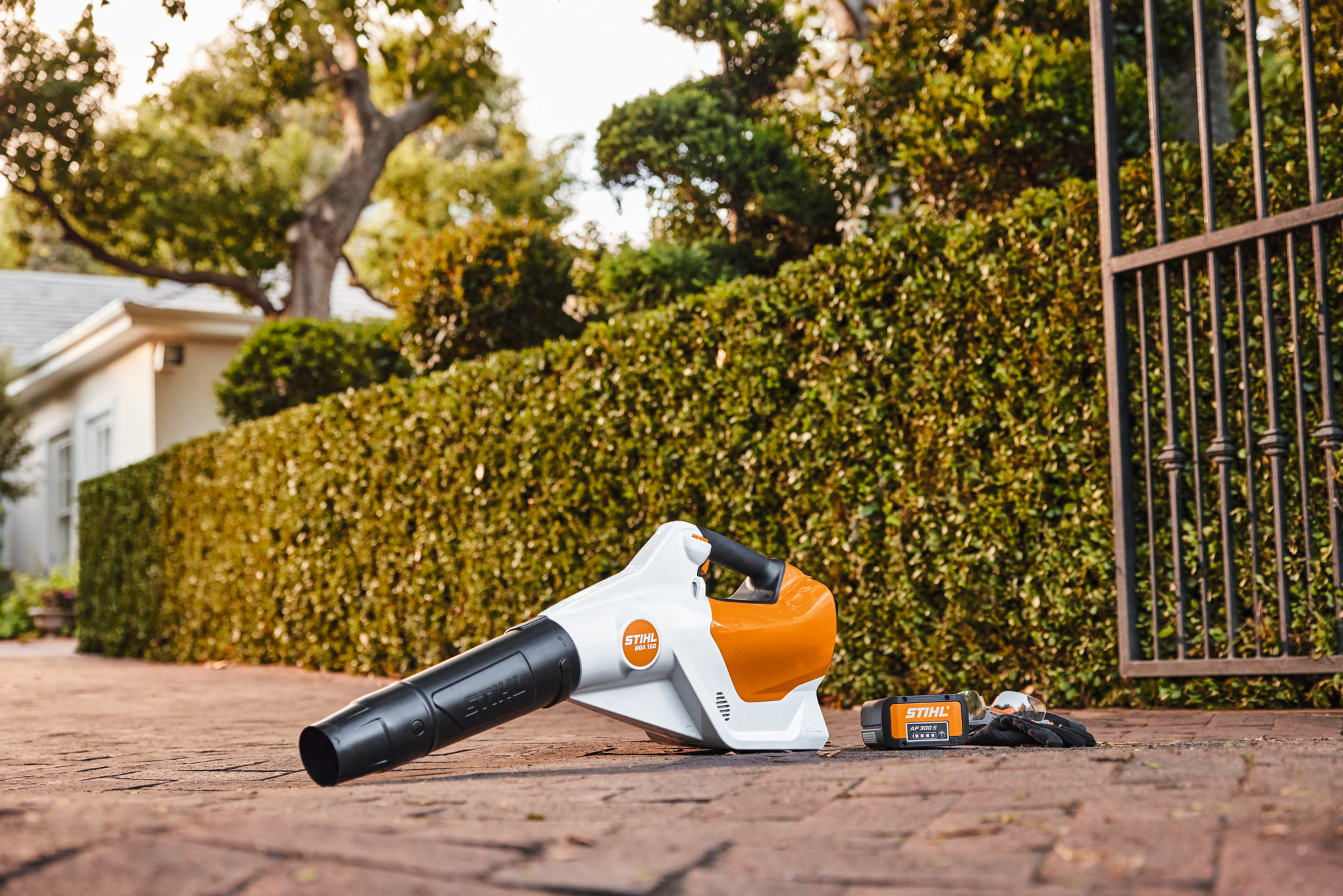 STIHL BGA 160 blower beside an AP 300 S battery in a manufacturer sample outdoor scene; the charger is not pictured.
